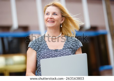 Close Up portrait, Happy and Smiling old senior business woman 60-65 years, using a laptop computer in New York city park, looking to up