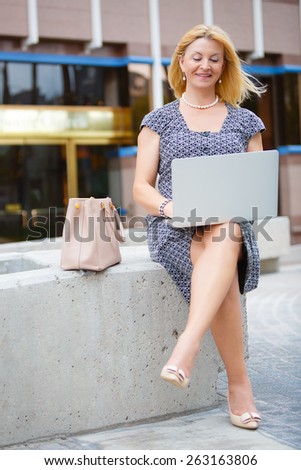 Happy and Smiling old senior business woman 60-65 years, using and typing keyboard on laptop computer in New York city park, looking to computer