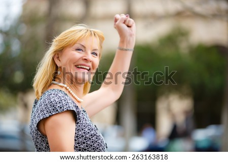 Close Up portrait, Happy and Smiling old senior woman 60-65 years, looking to up, with gesture on face and raised hand up with fist in New York city park