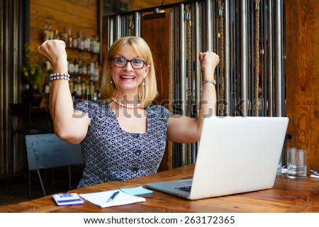 Close Up portrait Smiling old senior blonde business woman in the glasses, alone with laptop in summer cafe with gesture on face and raised hands up with fists