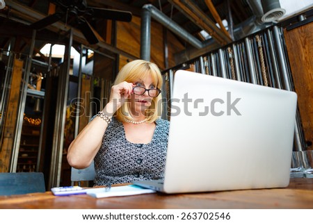 Old senior business woman with surprise emotion on face and big eyes, looking to computer laptop sitting in summer cafe place