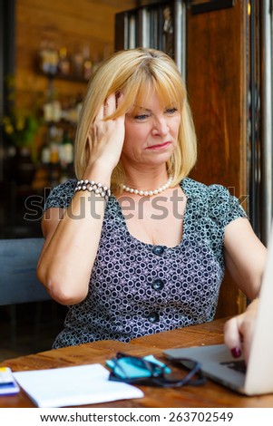 Old senior business woman with Headache emotion on face, looking to computer laptop sitting in summer cafe place