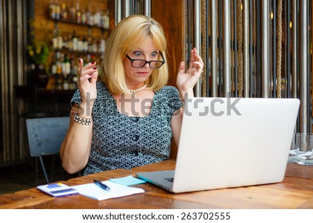 Old senior woman with glasses and surprised emotion on face and big eyes, looking to computer laptop sitting in summer cafe place