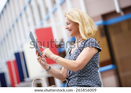 Portrait of happy smiling rich old business woman in city park using tablet pc computer reading ebook