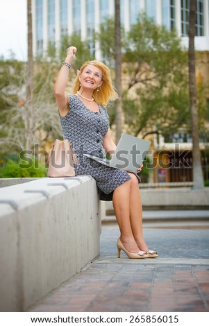 Happy and Smiling old senior business woman, using laptop computer in New York city park, looking to up, with gesture on face, emotion raised hand up