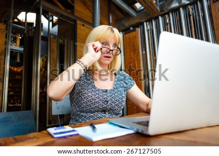 Smile Old senior woman 60-65 years with glasses and happy emotion on face, looking to computer laptop sitting in summer cafe place