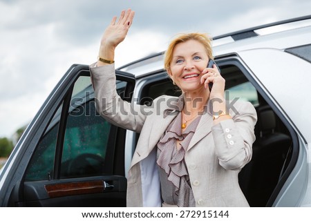 Close-up portrait with smiling happy old senior business woman 60-65 years, waving his hand and talking on the phone on car background