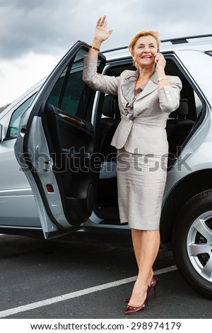 Trendy attractive senior old business woman 55-65 years with a lovely charming smile, wearing stylish suit, waving his hand and talking on the mobile phone, Positive human emotion, facial expression