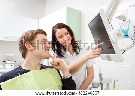 Young man on a review of a dentist, sitting in a chair. Dentist Explaining X-Ray on computer for patient in a dental clinic