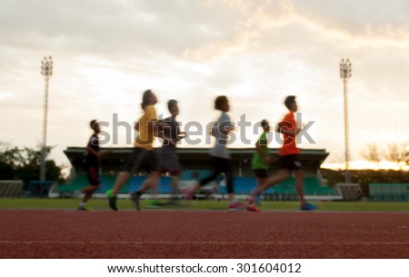 group running on race track on soccer stadium, sunset