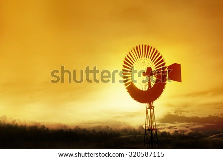 Old windmill used to pump water for cattle on a ranch or farm lit by warm glow of the setting sun.