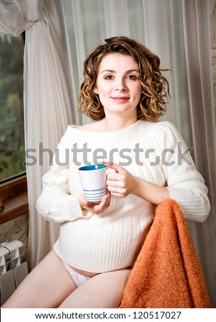 Pregnant woman drinking milk in the room sitting on a chair, Happy pregnant woman drinking milk