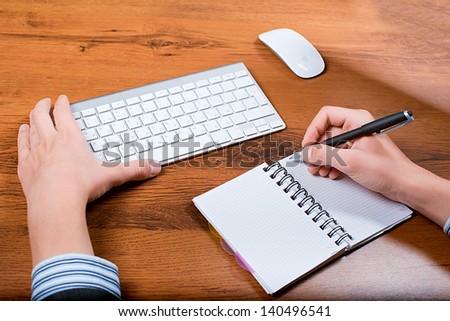Close-up of a businessman in office . Businessman writing in notebook. Very slim keyboard for your computer
