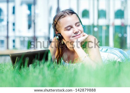 girl listens to music on headphones.  Female student girl outside in park listening to music on headphones while studying. Schoolgirl working on a laptop