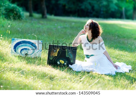 Beautiful girl with paintings on nature. Exhibition of paintings at the park. Artist with pictures