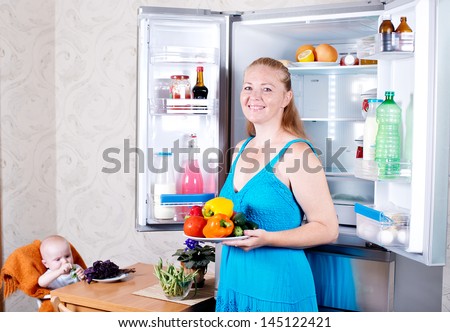 Young mother with a child takes food out of the fridge. Storing food in the refrigerator