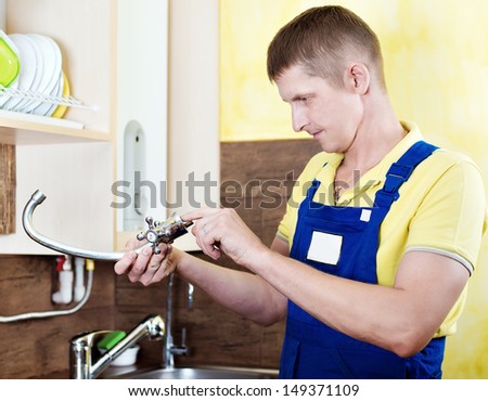Replacing the faucet in the kitchen. Plumbing works at home. Smiling handsome plumber with an adjustable wrench