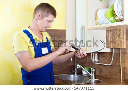 Replacing the faucet in the kitchen. Plumbing works at home. Smiling handsome plumber with an adjustable wrench