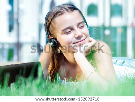 girl listens to music on headphones. Female student girl outside in park listening to music on headphones while studying. School Girl working on a laptop
