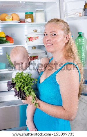 Young mother with a child takes food out of the fridge. Storing food in the refrigerator. A child in the arms of mother.