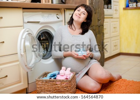 Happy pregnant woman washes baby clothes. Pregnant woman is getting ready for the maternity hospital, packing baby clothes