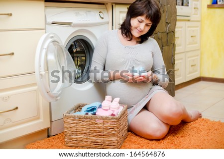 Happy pregnant woman washes baby clothes. Pregnant woman is getting ready for the maternity hospital, packing baby clothes