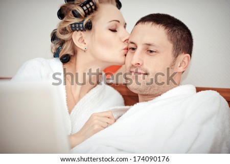 Young couple working at home in bed, using laptop, man and woman lying on the bed watching the laptop