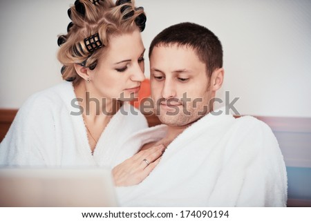 Young couple working at home in bed, using laptop, man and woman lying on the bed watching the laptop