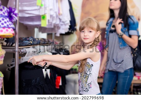 Cute beautiful little girl with her mother to buy clothes in shop