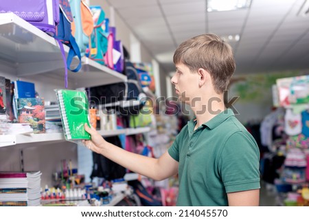 Buying school supplies at the supermarket. The young man buys a notebook in the store