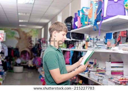 Buying school supplies at the supermarket. The young man buys a notebook in the store