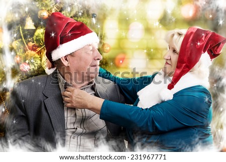 Happy beautiful elderly couple celebrating new family, holidays, christmas, age and people concept - happy senior couple in santa helper hats sitting on sofa over living room