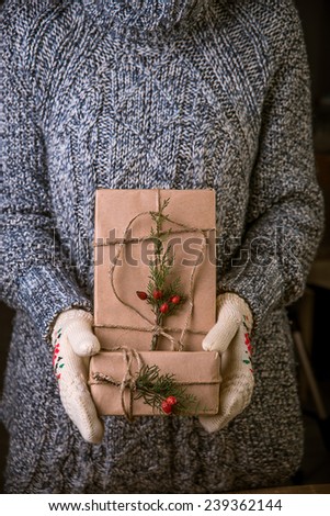 Hands in mittens holding gift box. Christmas gift wrapped in brown paper and twine held in hands with mittens
