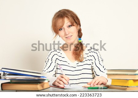 Charming  girl sitting at table with books studying writing in notebook