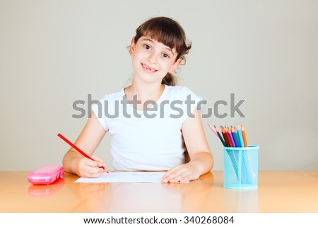 Cute little girl with red sketch pen is drawing at kindergarten