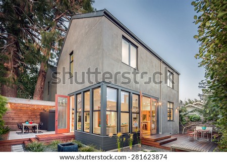 Contemporary home at twilight with wooden terrace, seating arrangement and lawn.