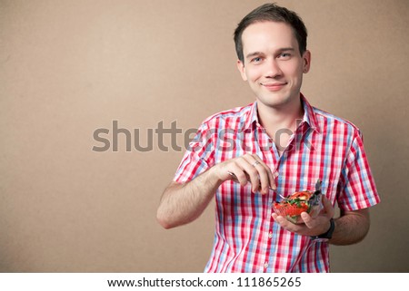 Slim handsome boy eating salad over wooden background. studio shot