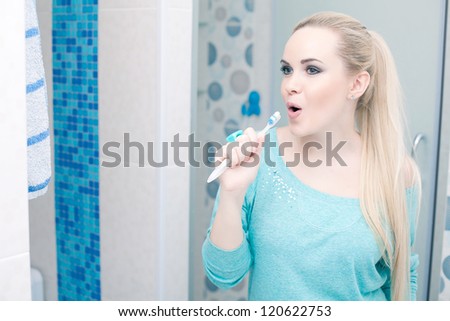 Beautiful pregnant lady having fun: blonde holding her toothbrush and singing a song. Indoor shot.