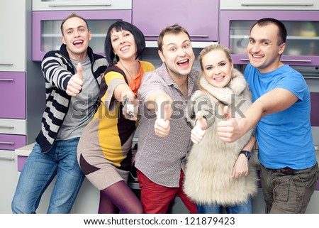 Five close friends enjoying a social gathering together and showing thumbs up happily at home (kitchen room). Indoor shot.