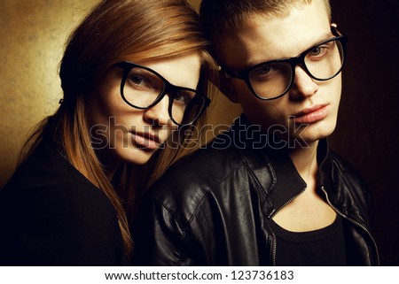 Portrait of gorgeous red-haired fashion twins in black clothes wearing trendy glasses and posing over golden background together. Studio shot.