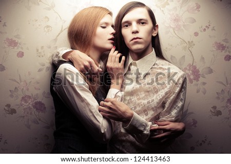 Portrait of beautiful long haired people in vintage style: handsome boy with brown hair and whispering gorgeous red-haired girl posing together. Studio shot.