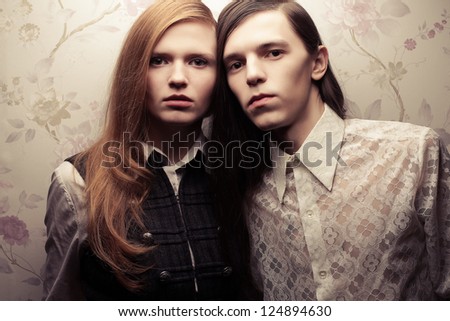 Portrait of beautiful long haired people in vintage style: handsome boy with brown hair and gorgeous red-haired girl posing together. Studio shot.