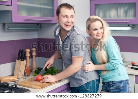 Portrait of a modern romantic couple preparing a meal (vegetable salad) in their well designed kitchen and looking at somebody or something. Woman (wife) is pregnant. Indoor shot