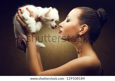 Portrait of two playing friends: fashionable model with sexy red lips holding her white little chinese crested dog. Both posing over golden background. Studio shot