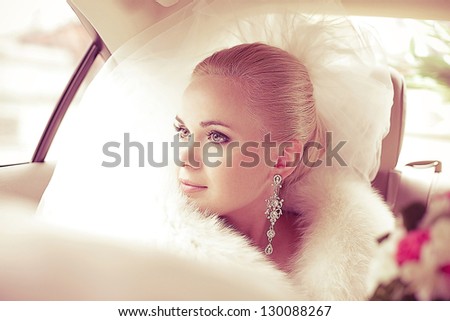 Portrait of a beautiful blonde bride sitting in the wedding car and looking at somebody or something through the window. Wedding day. Daylight