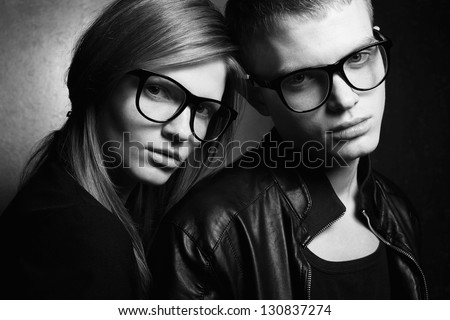 Portrait of gorgeous red-haired fashion twins in black clothes wearing trendy glasses and posing over golden background together. Black and white (monochrome) studio shot.