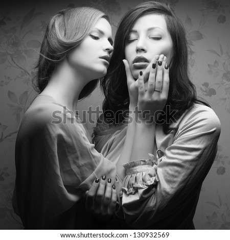 Retro portrait of two gorgeous women (girlfriends) kissing in great dresses in a hotel room. Vintage (Hollywood) style. Film noir. Old classic movie. Black and white (monochrome) studio shot