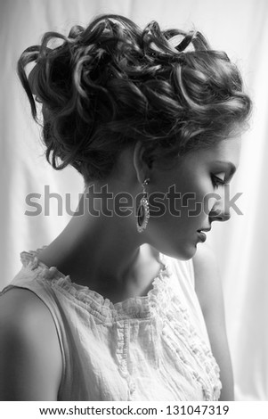 Emotive arty portrait of fashionable queen-like young woman in white vintage dress posing over white curtain background. Perfect retro hairdo. Close up. Profile. Black & white (monochrome) studio shot
