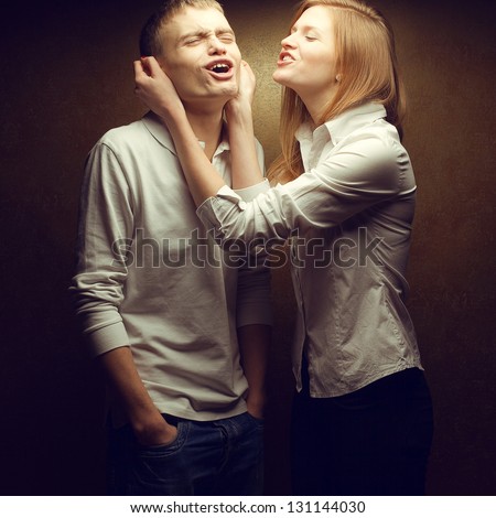 Emotive portrait of gorgeous red-haired (ginger) fashion twins in white shirts playing and laughing over golden background together. Sister pulling brother\'s ears. Studio shot.