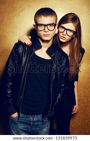 Portrait Of Gorgeous Red-Haired Fashion Twins In Black Clothes Wearing Trendy Glasses And Posing Over Golden Background Together. Perfect Hair. Natural Make-Up. Perfect Skin. Studio Shot.